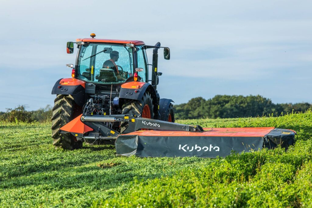 Tracteur Kubota M5002 équipé d'une faucheuse arrière en action dans une exploitation.